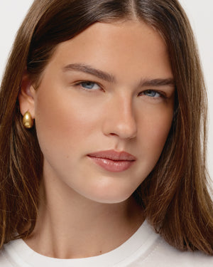 Close-up of a person with long brown hair wearing gold earrings against a neutral background