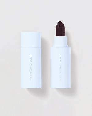 White cosmetic stick with dark berry applicator on a light beige background