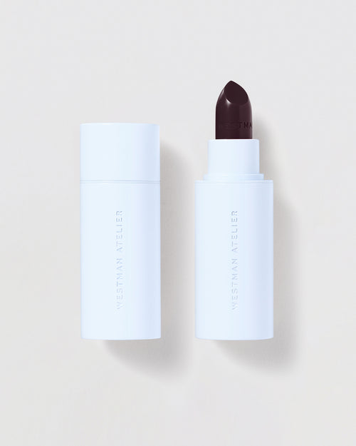 White cosmetic stick with dark berry applicator on a light beige background