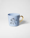 A light blue ceramic mug with a gold handle and a black and red floral line-art design on the side, set against a plain light gray background.