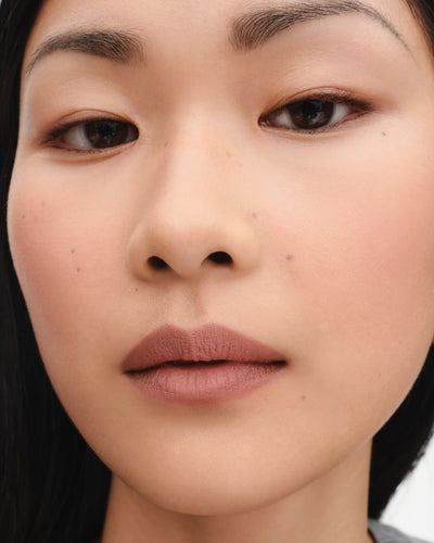 Model wears lipstick in shade Mimi (tawny beige).