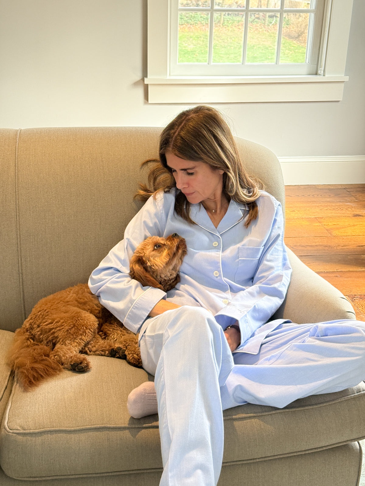 Woman in blue pajamas sitting on a couch with a dog.