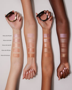 Three arms with makeup swatches on a grey background