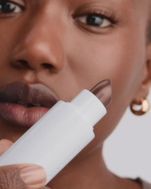 Model applies brown lipstick.
